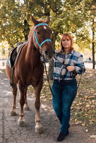 A woman stands near a horse. Farming, horseback riding. Autumn Park