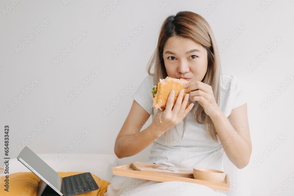 Asian Thai woman having breakfast on white bed while working, using tablet spending time at home alone on chilling day. Asian Thai woman having breakfast on white bed while working, using tablet spending time at home alone on chilling day.