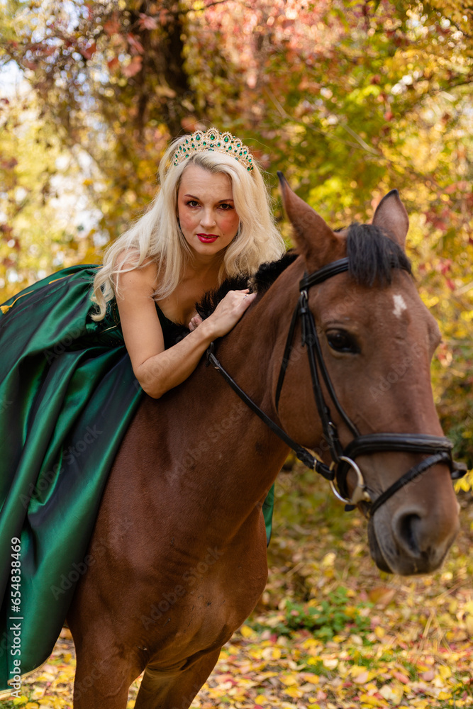 Fototapeta premium A woman in a long dress sits on a horse. Autumn forest, horse breeding