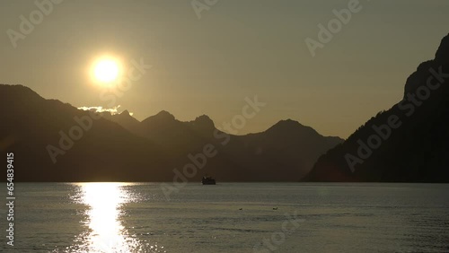 The boat sails in the rays of the setting sunThe sun sets behind the mountains above the lake. Evening in the mountains. Sunset on the lake among the Alps. photo