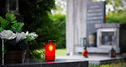 Close up of a red burning candle and flower decoration on the grave. Symbol of remembrance of our deceased relatives. Cemetery in the Czech Republic. All Souls' Day concept. All Saints Day photo