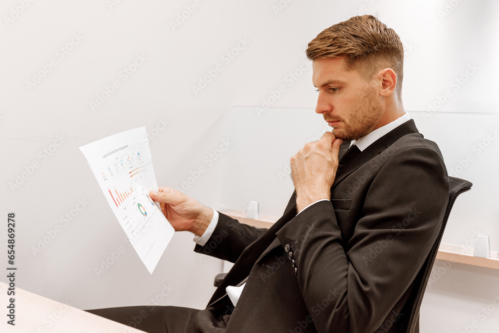 Stressed young Caucasian businessman sees incorrect information in paper document working from office Stressed young Caucasian businessman sees incorrect information in paper document working from office