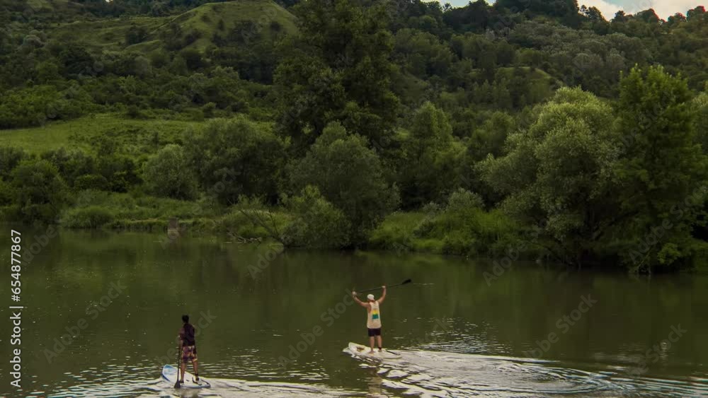 Aerial view of two adults silhouette on paddleboarding doing stand up paddle water sport activity on a wild river. Healthy lifestyle outdoor activity 