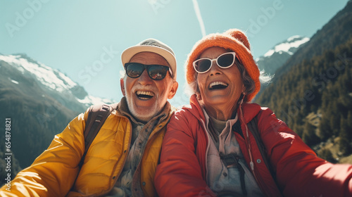 Happy elderly couple laughing on a snowy mountain on a sunny day. They wear warm hats and sunglasses for their excursion, enjoying their retirement and free time #654878821