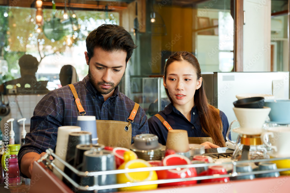 Young barista husband and wife own a small business that runs a coffee shop. Prepare coffee for customers to order at shop. A man and woman stand behind the counter preparing drinks in a coffee shop. Young barista husband and wife own a small business that runs a coffee shop. Prepare coffee for customers to order at shop. A man and woman stand behind the counter preparing drinks in a coffee shop.
