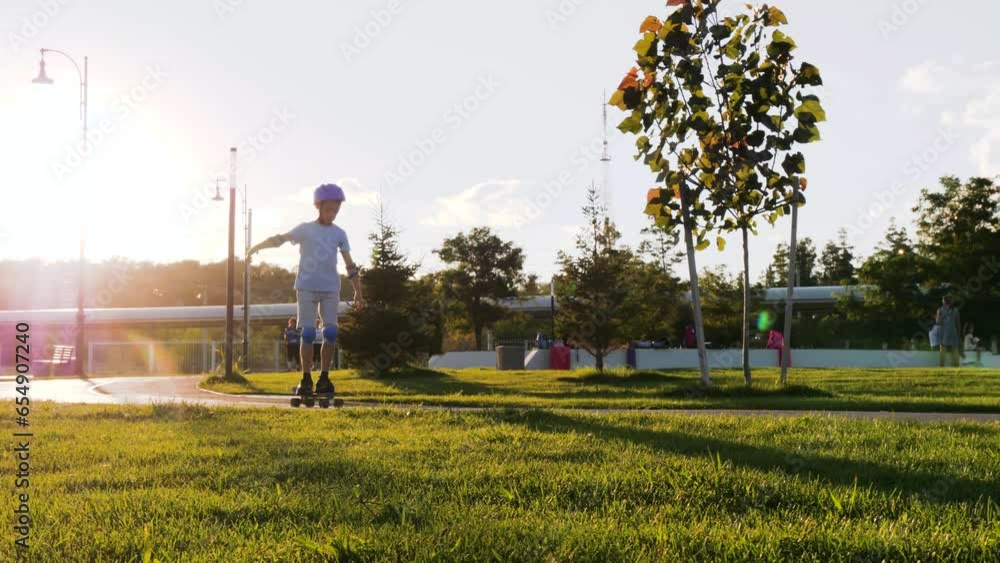 A happy kid in a safety helmet and suit skateboarding in the park. A boy skateboarding on the street in the sunset. Active recreation of children. a family, a child in a park with green grass. A happy kid in a safety helmet and suit skateboarding in the park. A boy skateboarding on the street in the sunset. Active recreation of children. a family, a child in a park with green grass.