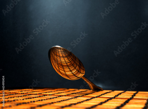 shot of the convex part of a suspended silver spoon reflecting the linear design of the underlying plane, illuminated by a beam of light from above, against a black background