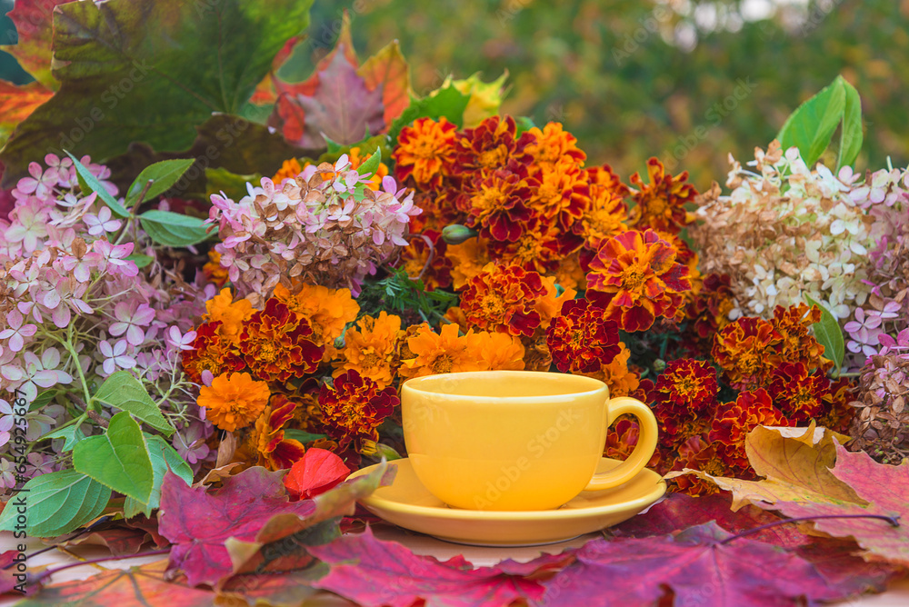 Autumn gardening concept; Yellow cup of tea, bunch of flowers and maple leaves in the garden Autumn gardening concept; Yellow cup of tea, bunch of flowers and maple leaves in the garden