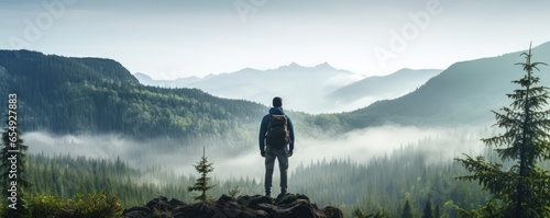 A lonely man enjoys the view of the summer mountains while he standing on a mountain peak. Hiking and digital detox concept. Contemplation of nature alone with your thoughts. Format photo 5:2.