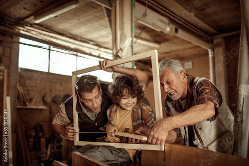 Multigenerational family of male carpenters teaching their youngest one the ways in a carpentry shop © Geber86