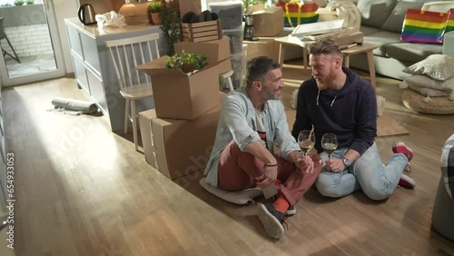 Young male gay couple having wine and taking selfies in their new apartment after moving in