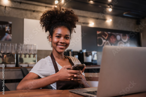 Cute young black female waitress barista using mobile phone and laptop with happiness in the cafe at restaurant.