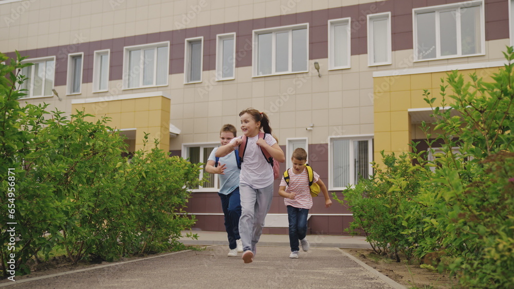 Joyful schoolchildren run holding hands across elementary school yard.