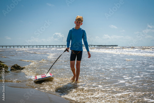 Photography Male child on beach pulling his boogie board while walking and splashing in the