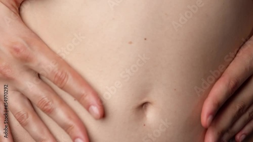 Closeup studio shot of beautiful caucasian woman body part, touching tummy belly button area with hands, soft skin.