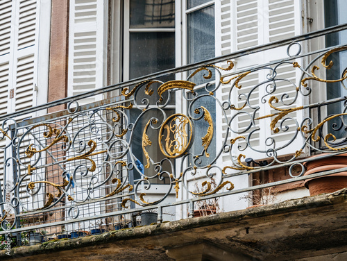 A captivating scene of a French balcony with an open window and golden protective railing, situated in an upscale French neighborhood.