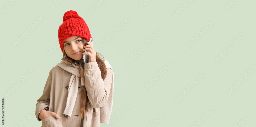 Cute little girl in winter clothes talking by mobile phone on light background with space for text