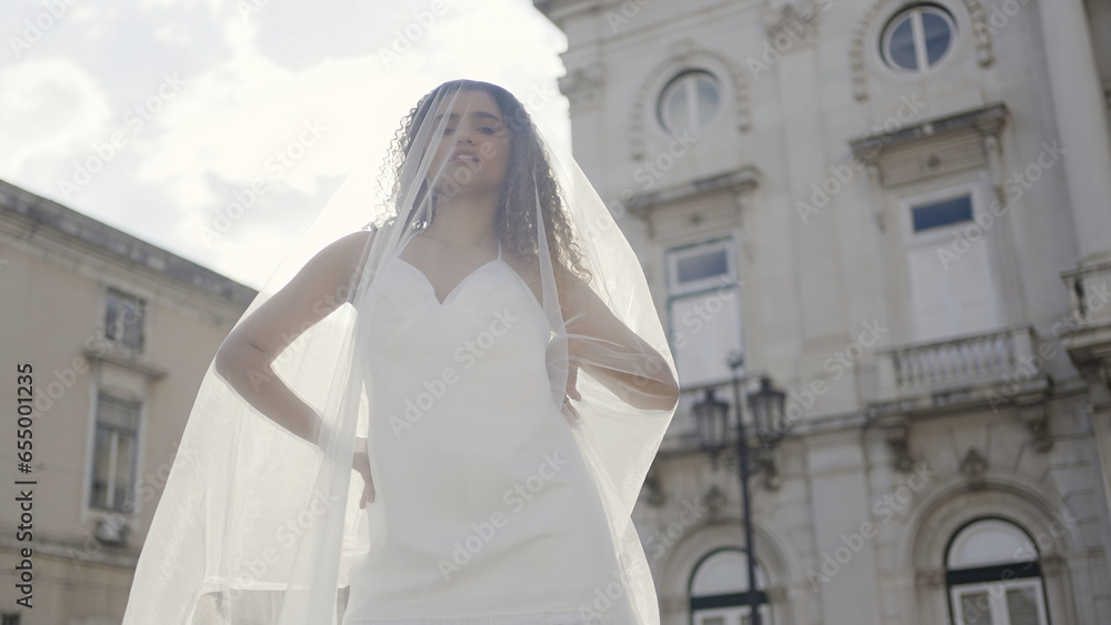 Elegant bride in short white dress and long veil. Action. Summer photosession in the old city street of a young woman with curly hair.