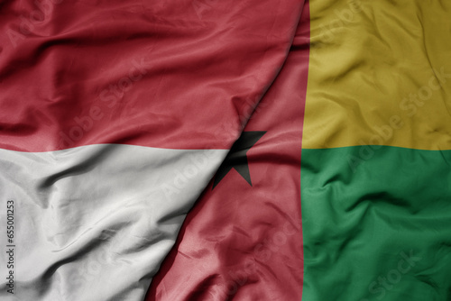 big waving realistic national colorful flag of indonesia and national flag of guinea bissau .