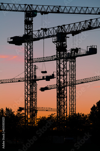 Silueta de conjunto de torres de grúas al atardecer en un terreno donde se están realizando obras de construcción de edificios residenciales.