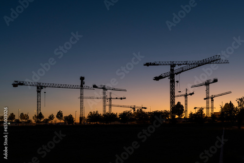 Silueta de conjunto de torres de grúas al atardecer en un terreno donde se están realizando obras de construcción de edificios residenciales. photo