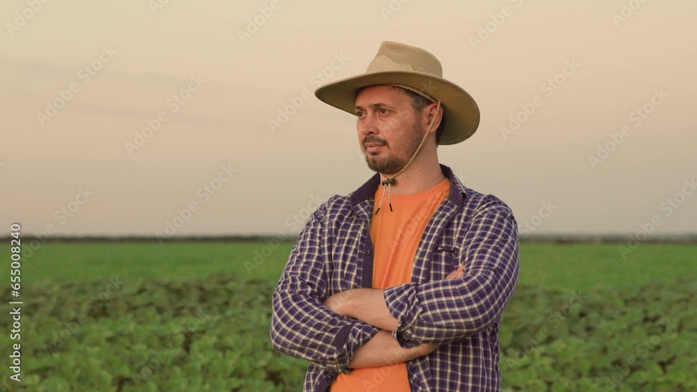 Farmer, businessman, with beard and hat, man looks into distance. Portrait of thoughtful senior farmer looks at camera. Senior Farmer smiling. Slow motion. Businessman in countryside, nature sunset