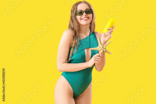 Beautiful young woman with sunscreen cream and starfish on yellow background