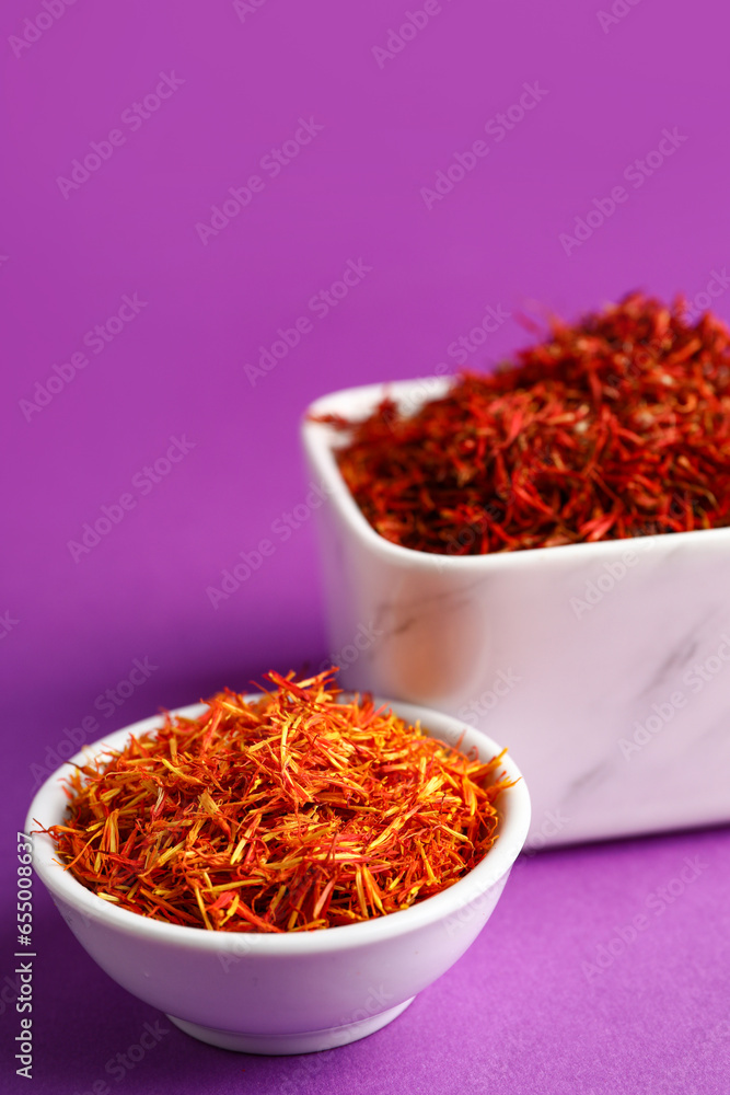 Bowls with pile of saffron on purple background Bowls with pile of saffron on purple background