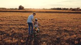 Father holds little daughter learning to ride bicycle in field on family holiday