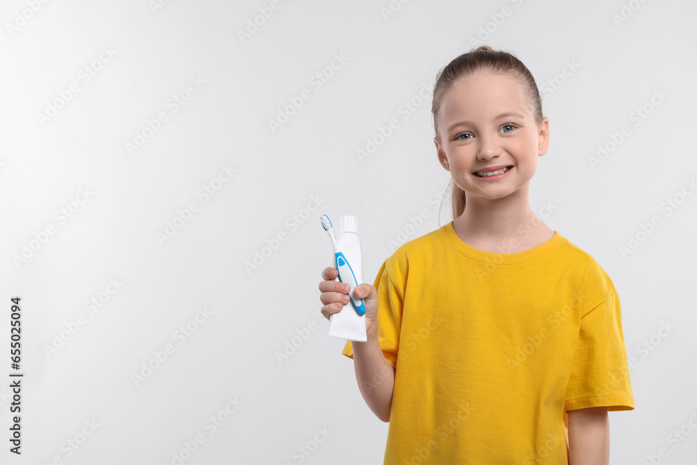 Happy girl holding toothbrush and tube of toothpaste on white background. Space for text Happy girl holding toothbrush and tube of toothpaste on white background. Space for text
