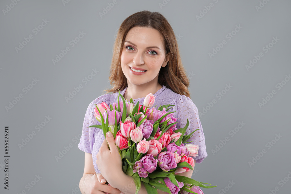 Happy young woman with bouquet of beautiful tulips on grey background