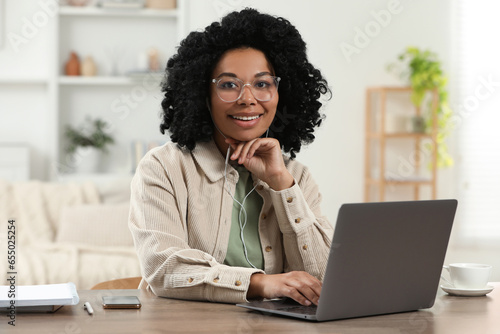 Happy young woman with laptop at wooden desk indoors
