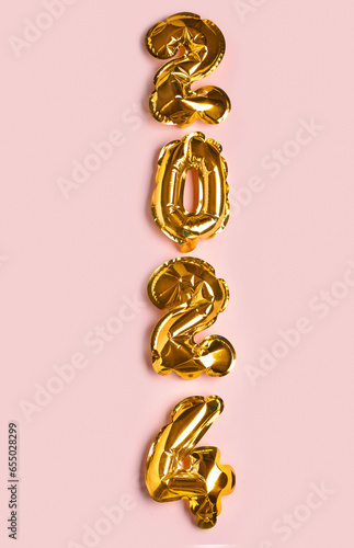 Golden foil balloons number 2024 on pink background. New year concept.