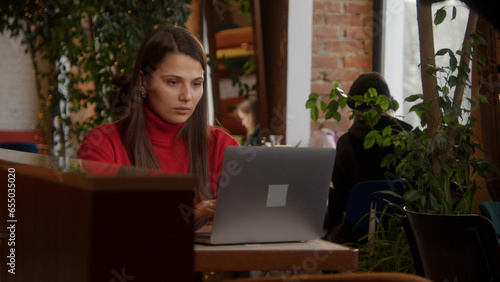 Beautiful woman is working at laptop in cafe. Stock footage. Stylish young woman is working at laptop in cafe. Beautiful woman is typing novel or working on laptop. Freelance