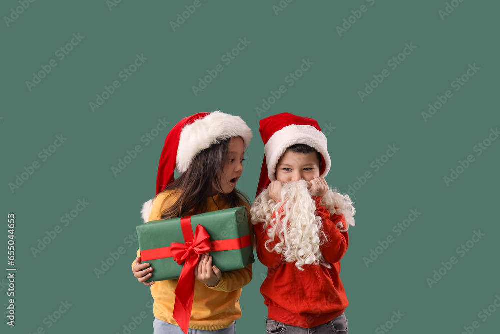Cute little children with Christmas gift and Santa Claus beard on green background Cute little children with Christmas gift and Santa Claus beard on green background