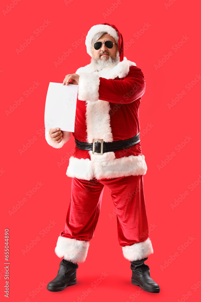 Cool Santa Claus with sunglasses and blank sheet of paper on red background Cool Santa Claus with sunglasses and blank sheet of paper on red background