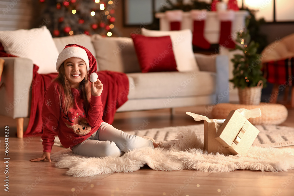 Obraz premium Cute little girl in Santa hat at home on Christmas eve