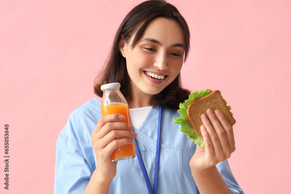 Young female doctor with bottle of orange juice and tasty sandwich on pink background Young female doctor with bottle of orange juice and tasty sandwich on pink background