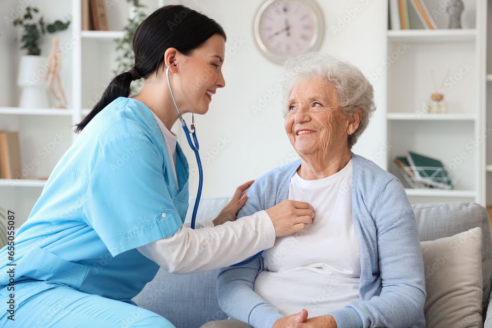 Fototapeta premium Female nurse hearing senior woman with stethoscope at home