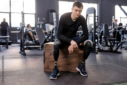full length portrait of serious sportsman with prosthetic leg sitting on fitness box and after workout, free time, spare time. lifestyle, tiredness