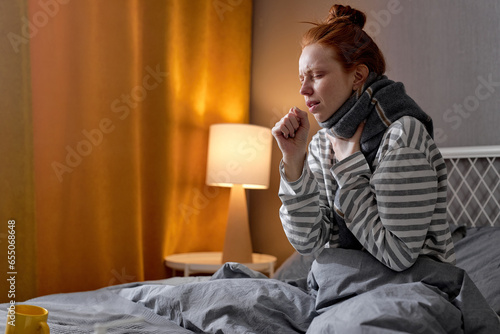 beautiful girl feels sick while sit on bed in bedroom. Attractive sleep young woman cover her mouth, feeling bad with fever and coughing after lying on bed at night at home. closeup side view portrait