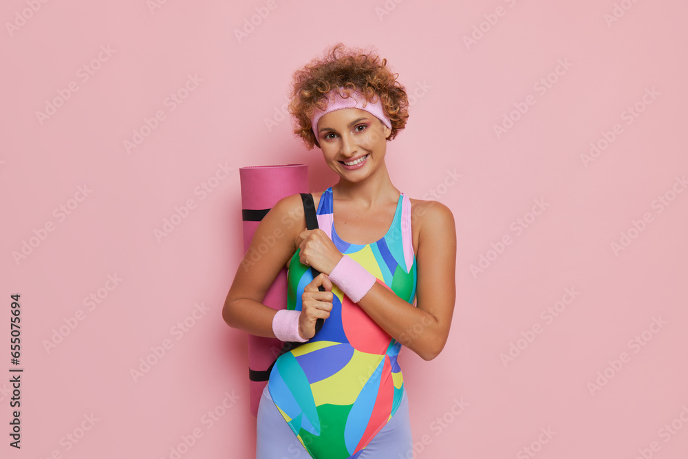 Pretty sports girl with short curly haircut carring pink yoga mat over her shoulder, sport lifestyle concept, copy space Pretty sports girl with short curly haircut carring pink yoga mat over her shoulder, sport lifestyle concept, copy space