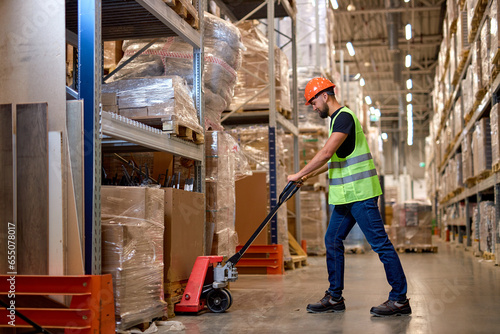 Young male warehouse worker carrying delivery to production stock using forklift. male staff in vest and orange helmet in place of work. Forklift driver stacking pallets with packs