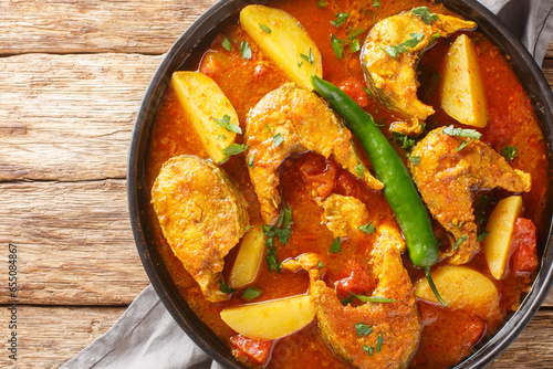Photography Machher jhol or machha jhola, is a traditional spicy fish curry in Bengali and Odia cuisines closeup on the plate on the wooden table