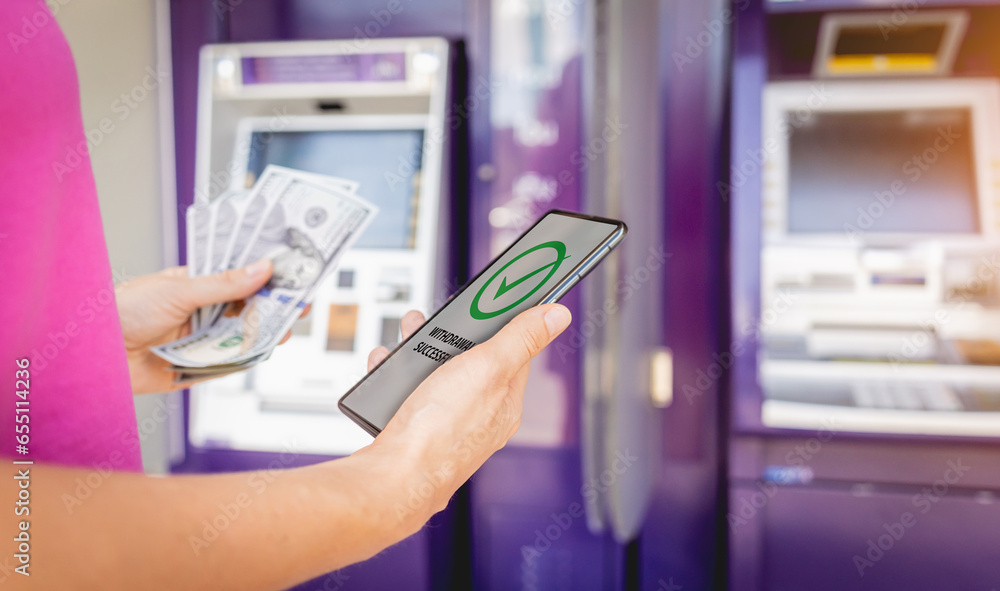 Young woman using the smart phone for cardless withdrawing the cash near the ATM Young woman using the smart phone for cardless withdrawing the cash near the ATM