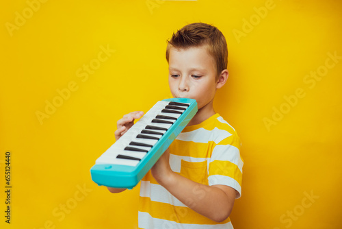 Cute child boy play the keyboard harmonica, yellow background photo