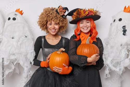 Fotografie Horizontal shot of two cheerful women stand closely to each other with orange pu