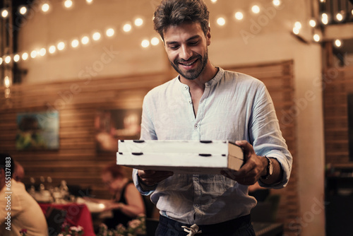 Evening Takeout: Man with Pizzas Exiting Pizzeria - Man in his 30s leaves a pizzeria at night with two pizzas. Ambient restaurant lights highlight the scene, showcasing the lively takeaway experience.