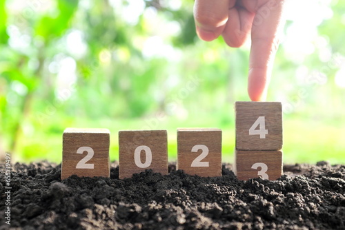 Human hand change year 2023 to 2024 in wooden blocks with growing plant at sunrise. Welcome new year 2024 and goodbye 2023 concept. photo