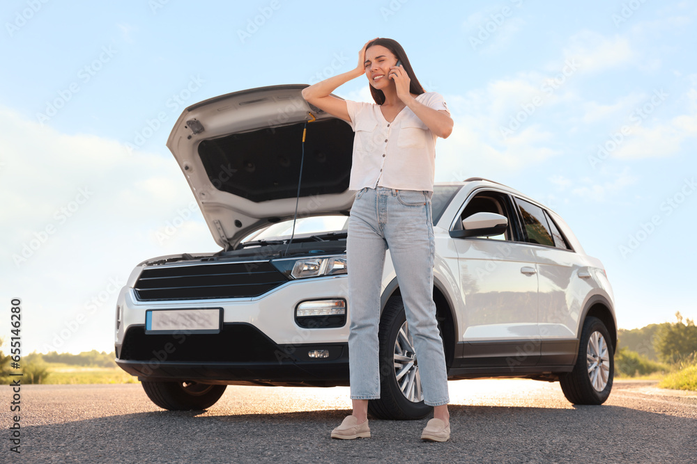 Stressed young woman talking on phone near broken car on roadside, low angle view Stressed young woman talking on phone near broken car on roadside, low angle view